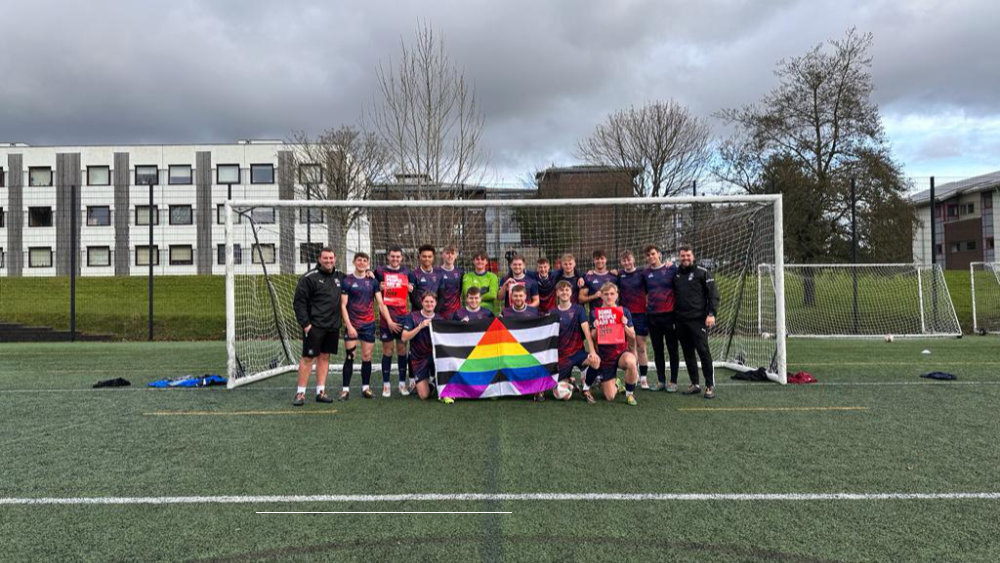 The Marjon football team posed in front of a goal while holding up an LGBTQ flag