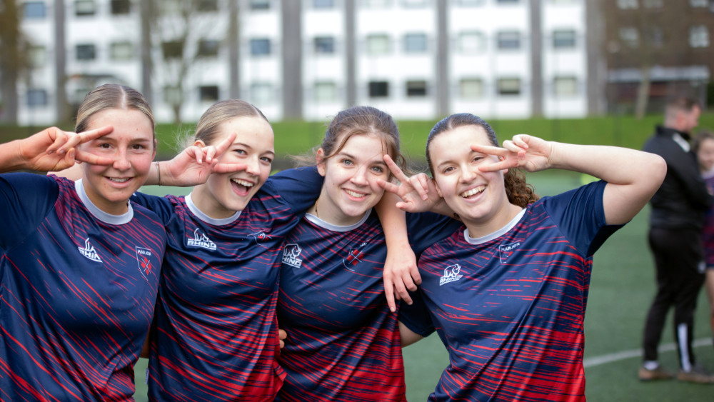 Four women in Marjon football kit pose while doing the V for Victory sign with their hands