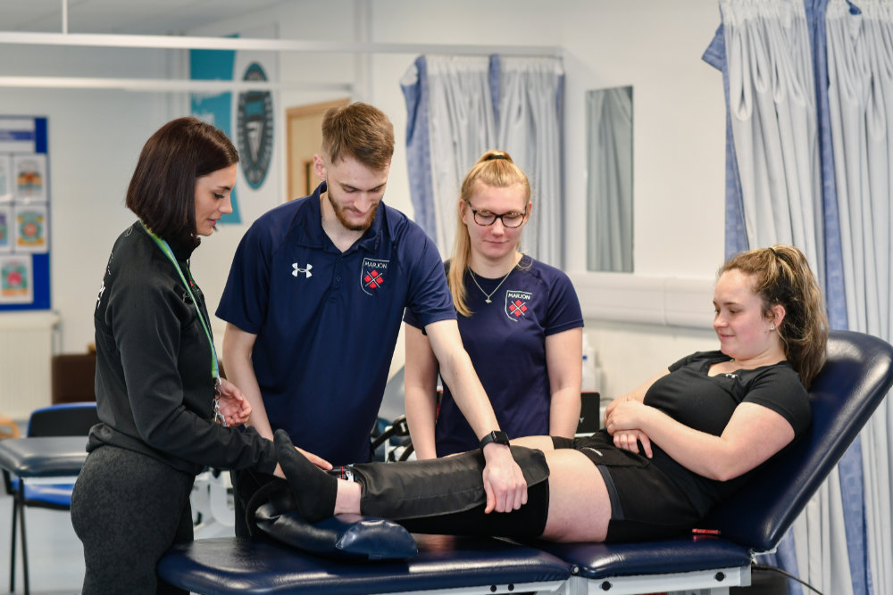 A woman has her leg examined by two Marjon students under the supervision of Beth Willment