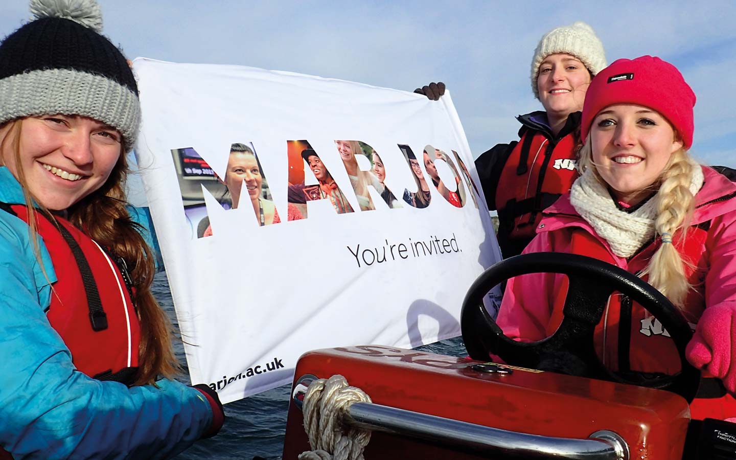 Three students holding a Marjon flag