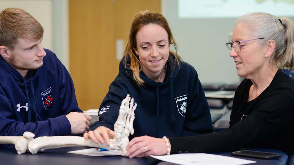 Lecturer explains anatomy to two students using a skeleton as a teaching aid