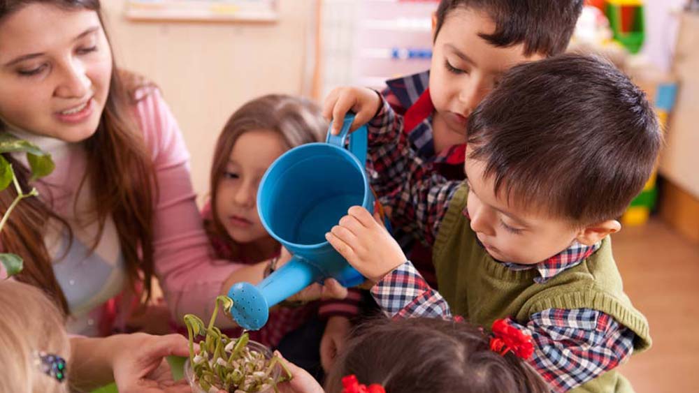 Early Years support worker encourages young children to water a plant