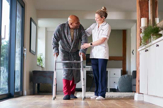 A physiotherapist assists an older man to use a walking frame