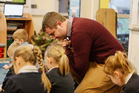 Primary school teacher listening to a pupil in class