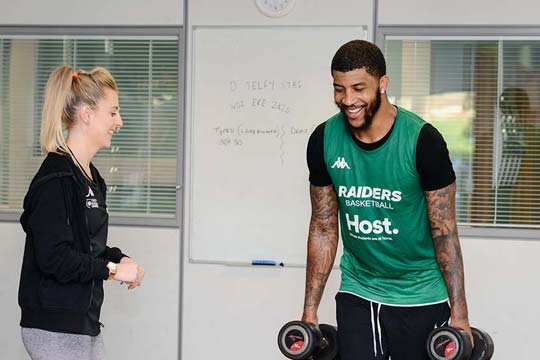 Student directs professional athlete who is lifting weights in the strength training lab