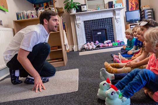 Small children look on engaged as Early Years teacher tells them a story