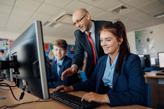 A teacher teaches two students who are doing computer work