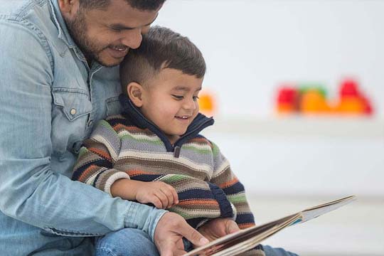 Young boy sits on his Dad's lap while they read together