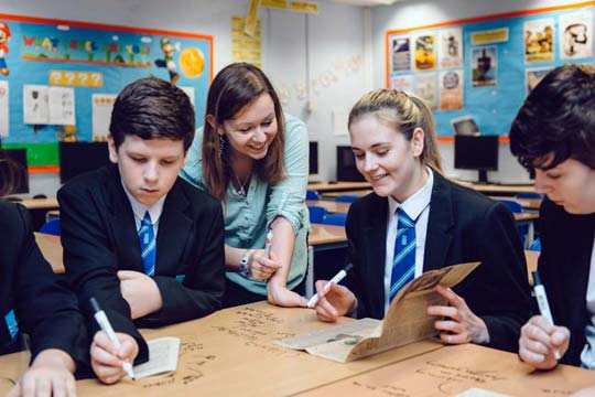 Teacher supports a group of pupils as they make notes while exploring old newspaper stories