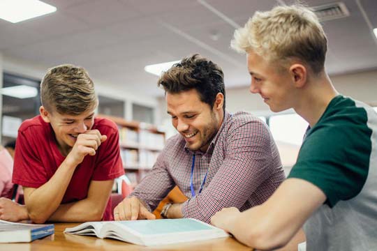 English teacher and two pupils laugh as they study a book together