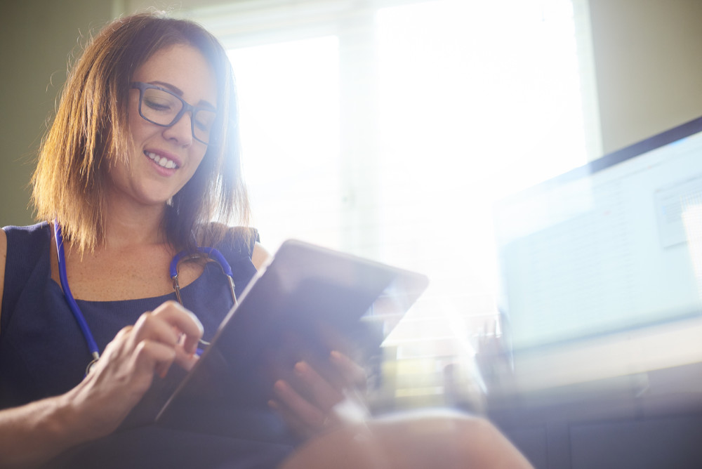 A female doctor sits looking at the screen of a tablet device and smiling