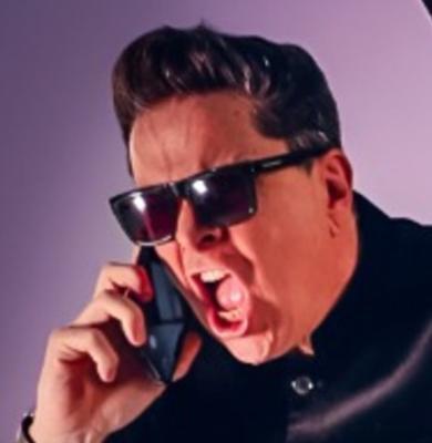 Dom Joly in dark glasses shouting into his mobile phone