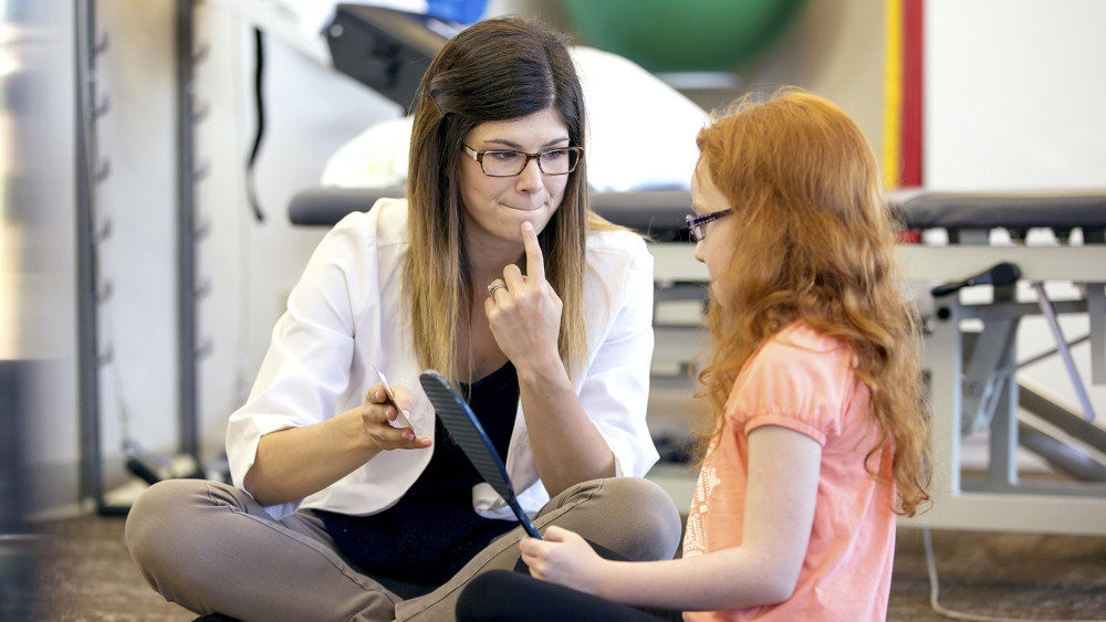 A speech and language therapist using sign language to talk to a young student