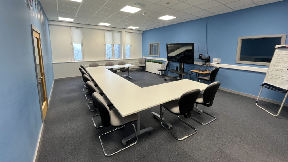 A large u-shaped table arranged with a TV in front of it in a space available for hire