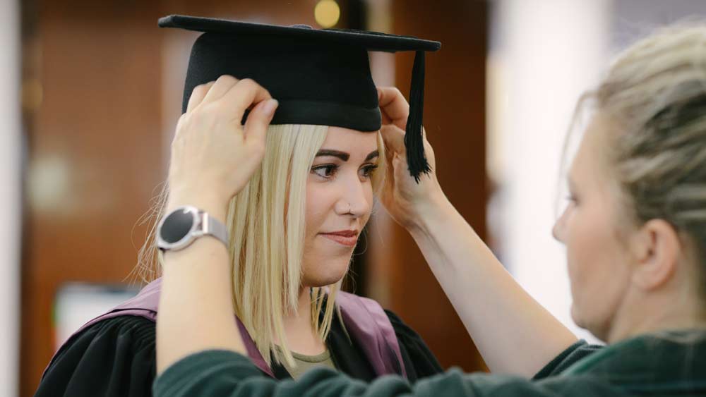 A student is fitted with their mortar board ahead of their Graduation