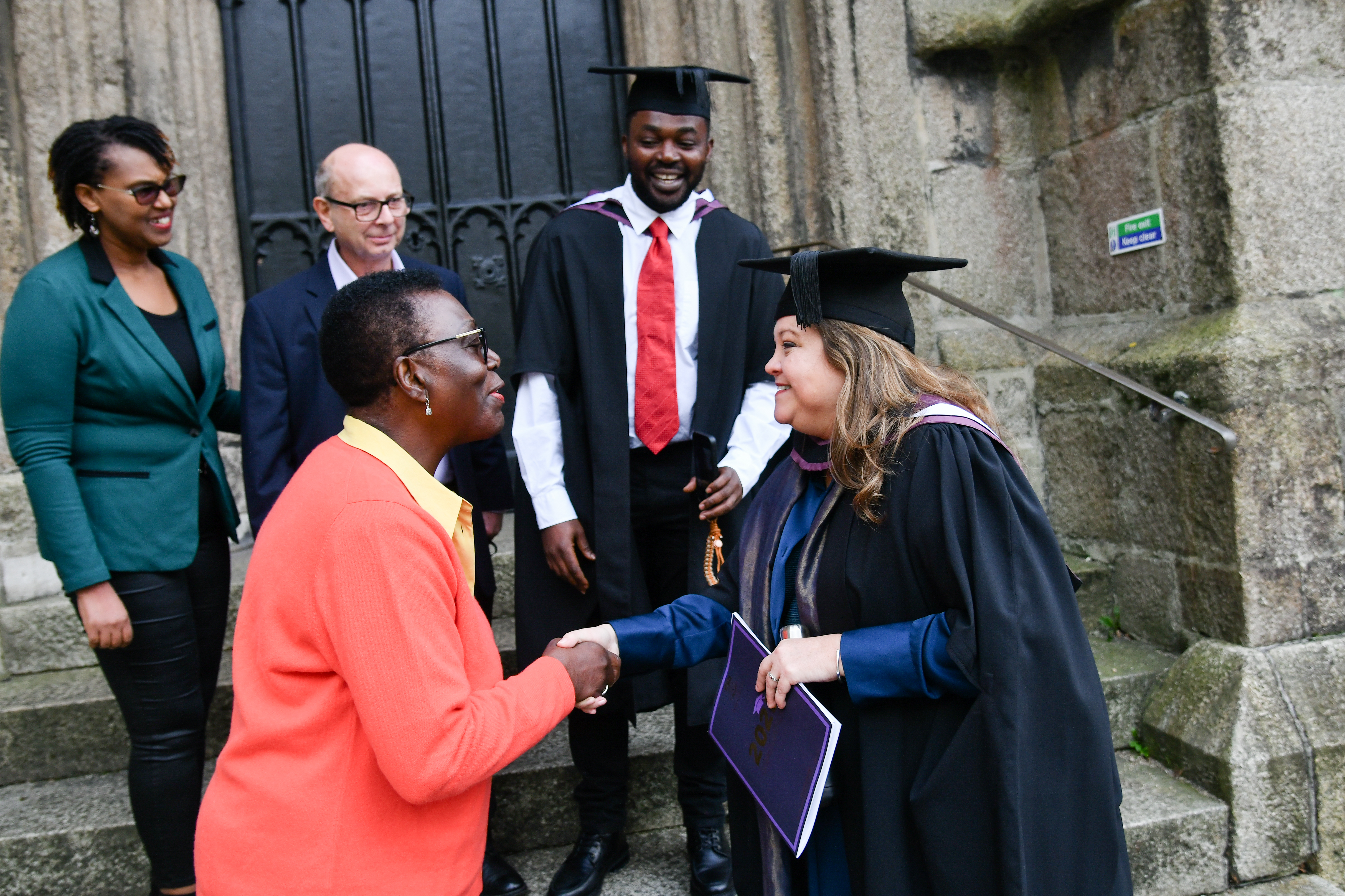 Lecturer and parent shaking hands in front of graduated student