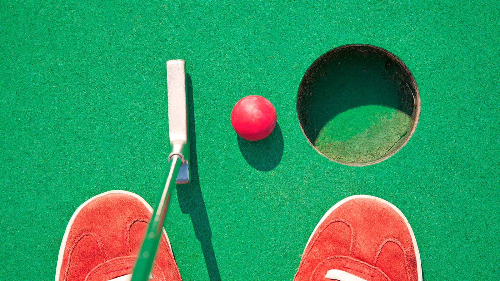 Looking down on putter and red golf ball by the hole
