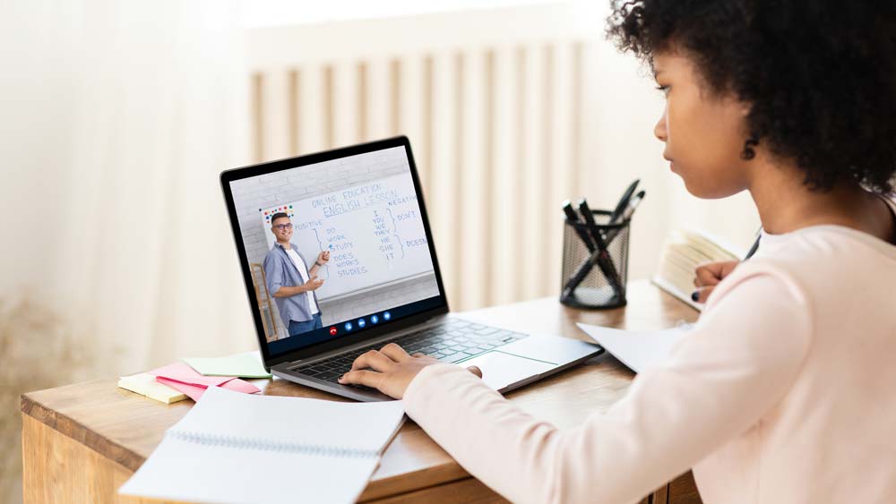 A pupil is watching a recorded lesson with their teacher on their laptop