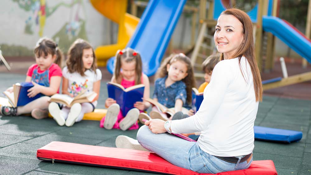 An Early Years Teacher looks at books with preschoolers in the playground