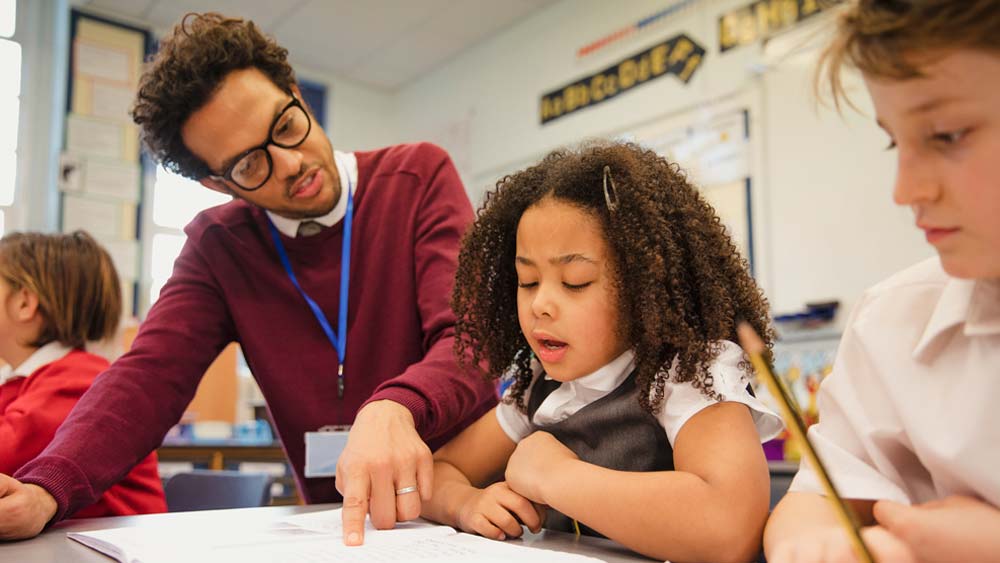 A teacher works with two pupils at their desk