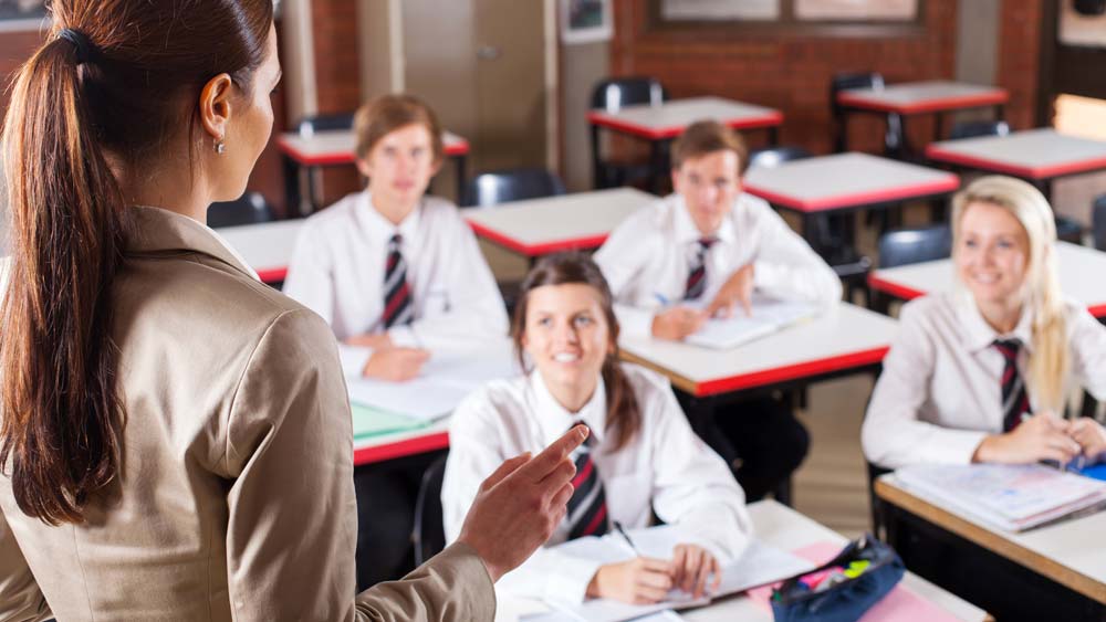Four teenage pupils focus on their teacher who is talking at the front of class