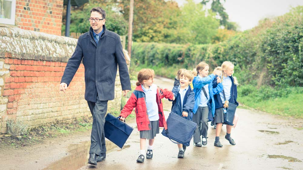 A teacher leads his class as they walk in a line outside