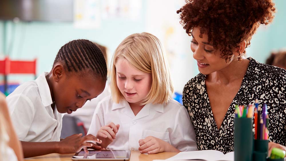 A teaching assistant sits with two children who are working