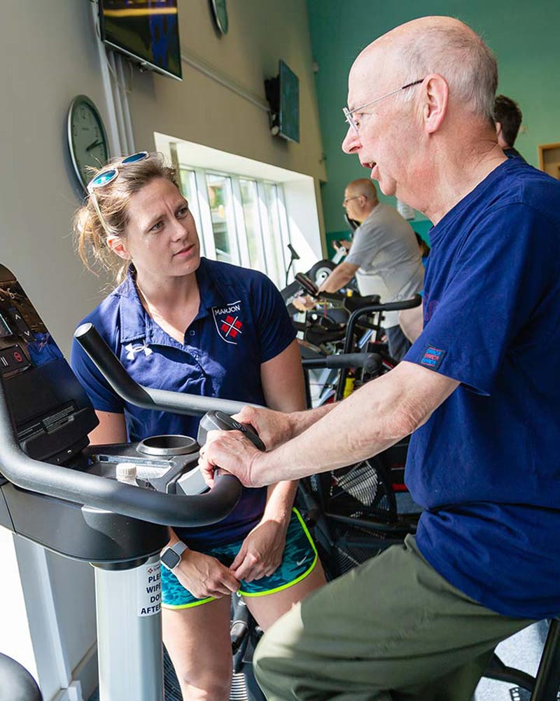 Trainer talks to a patient who is using an exercise bike