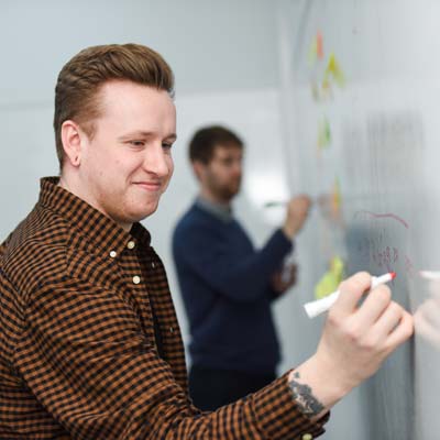 Two business students brainstorm on a whiteboard wall