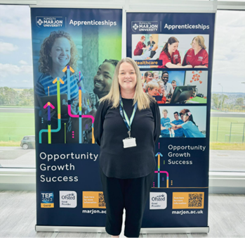 Jane Wickett, Apprenticeships Manager at Marjon, stands in front of two Apprenticeships-focused banners