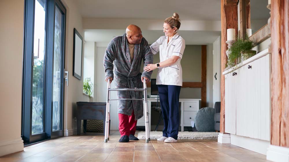 A physiotherapist assists an older man to walk with a walking frame
