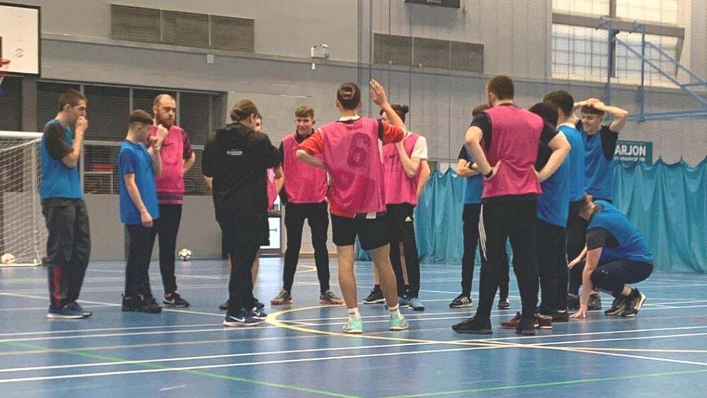 Students attending a practical football coaching session in the sports hall