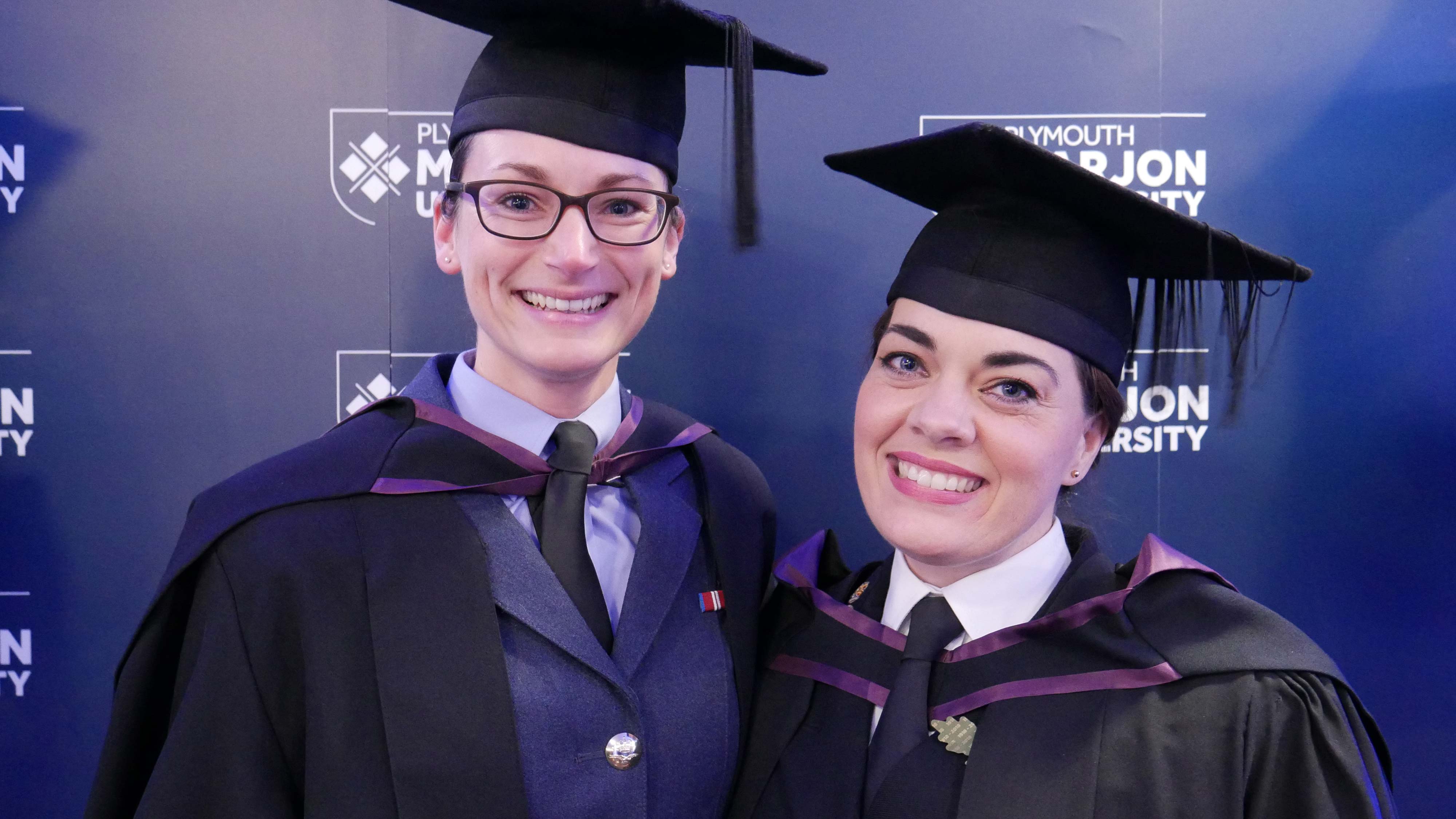 Two members of the armed forces in uniform and graduation robes 