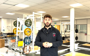 Researcher Tommy Bright standing in lab in front of set of colourful barbells