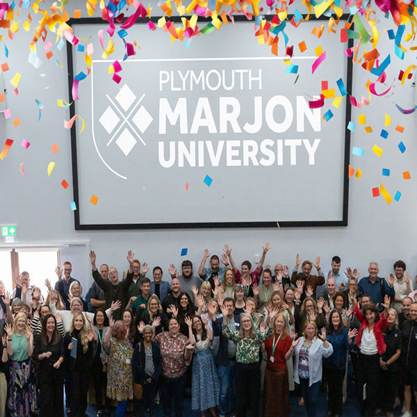 Group of staff raising their arms in lecture theatre with confetti from ceiling