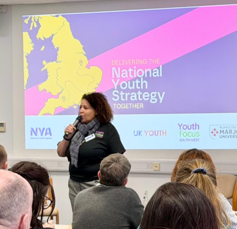 Woman standing in front of projector screen holding microphone