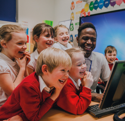 Group of smiling students with teacher gathered around a screen