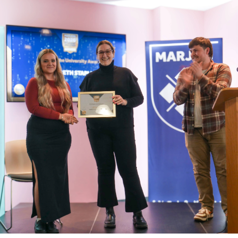 Award winner stands centre stage clapped by presenter and student union president