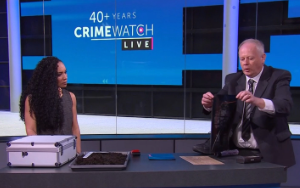 Crimewatch presenter at a desk while Dave Moore demonstrates materials