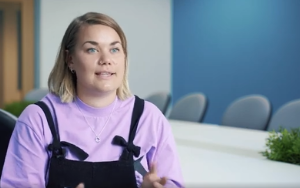 Young woman with blond bob, lilac t-shirt and dungarees talking to camera